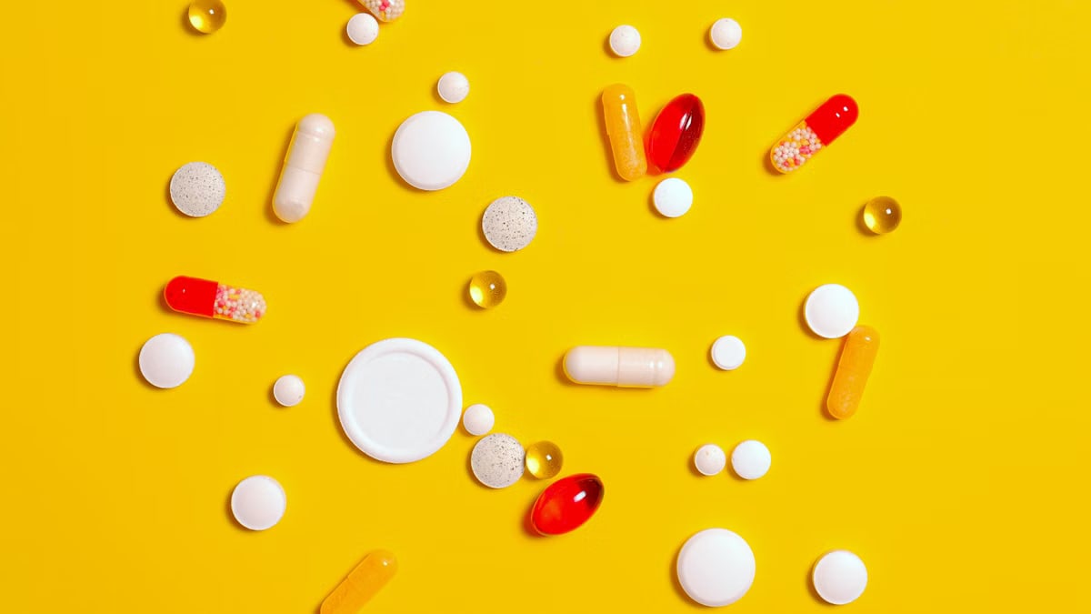 A variety of pills and capsules scattered on a vibrant yellow backdrop, emphasizing health and medicine.