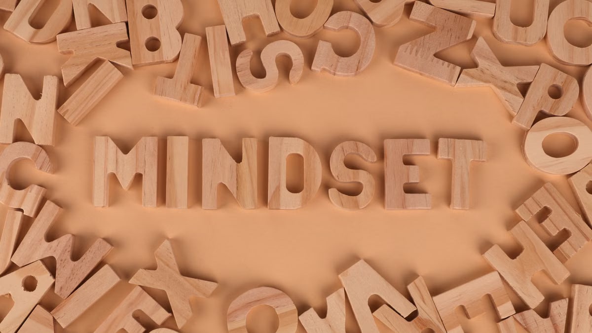 Wooden alphabet letters arranged to spell 'Mindset' on a peach background.